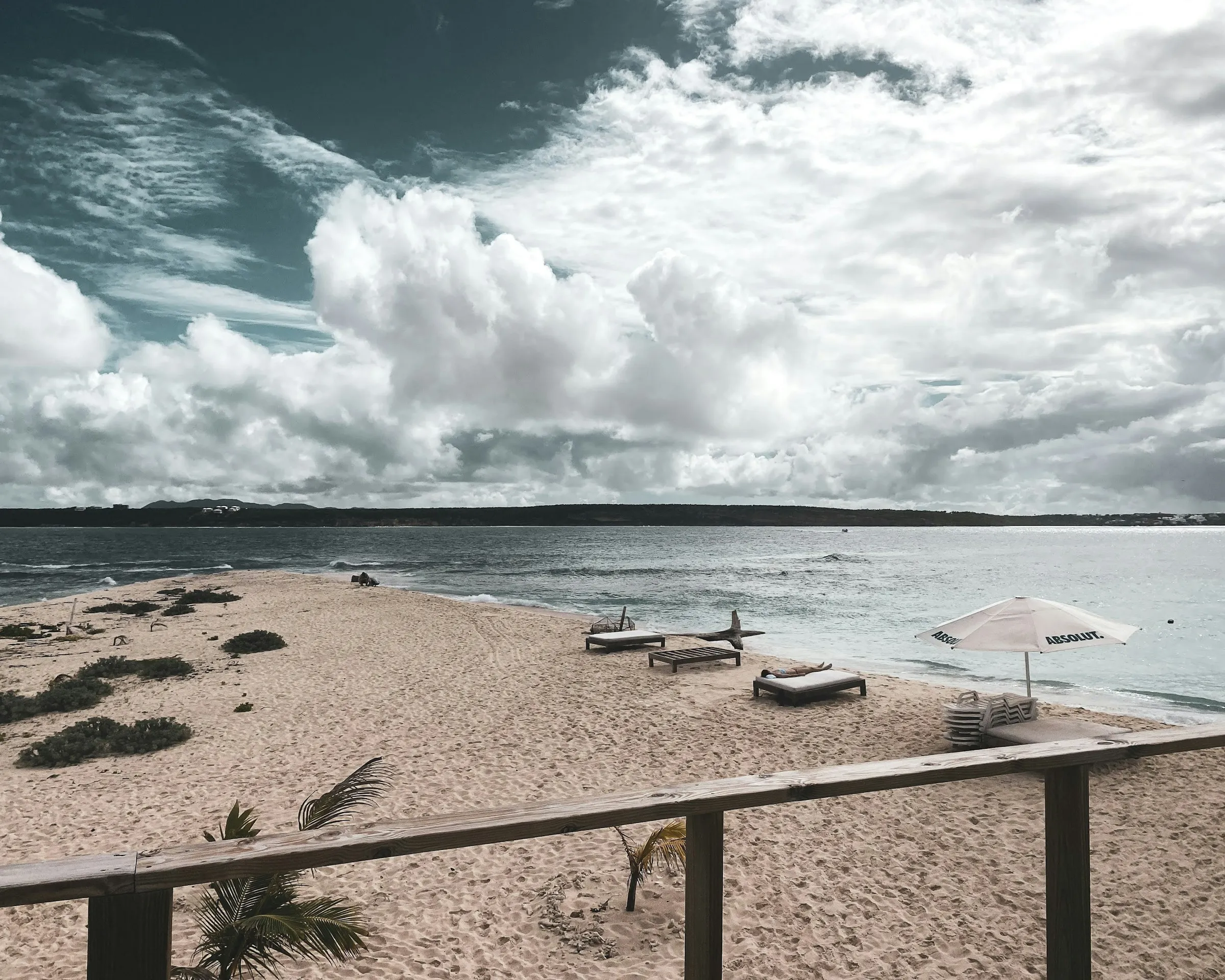 Empty beach loungers under an umbrella on a quiet Anguilla shoreline.