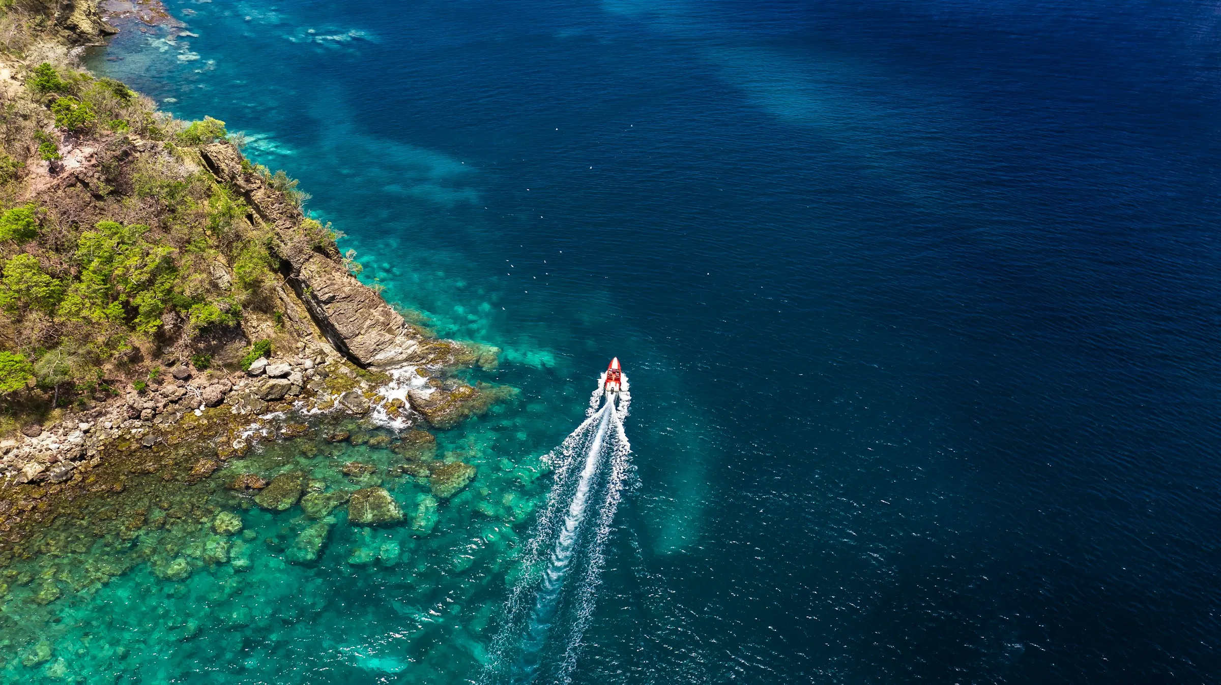 Small powerboat cruising calm clear water along a tropical rocky coast.