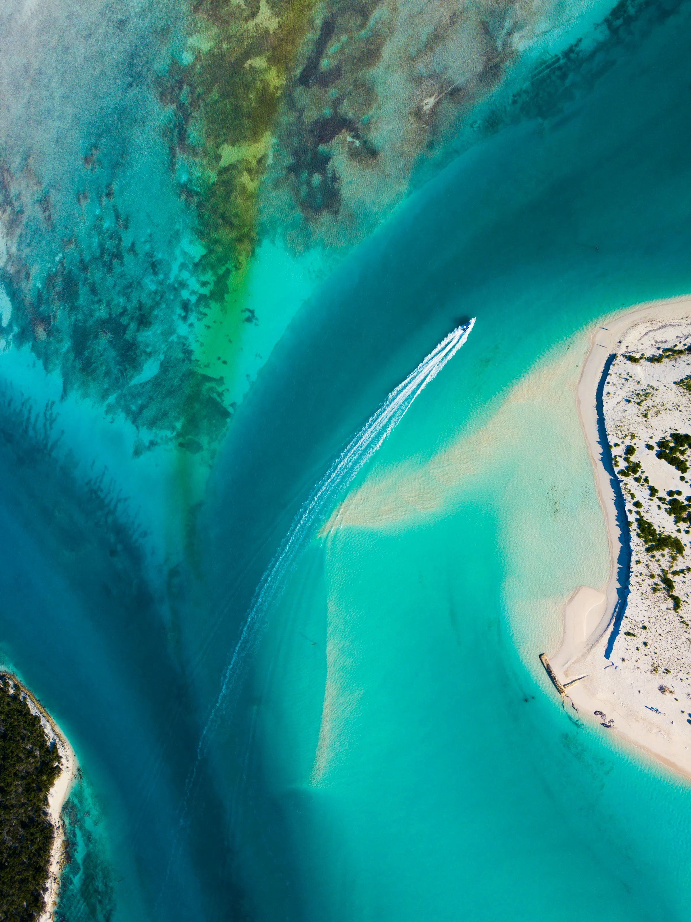 Aerial view of a private speedboat crossing turquoise Caribbean waters between sandbars.